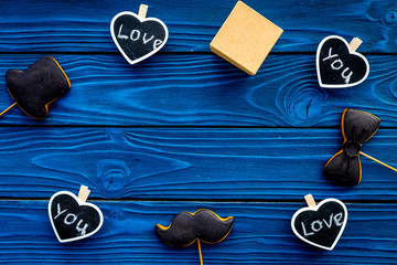Gift for man on birthday. Gift box among cookies in shape of moustache, hat, bow tie and hearts with lettering love you on blue wooden background top view copy space