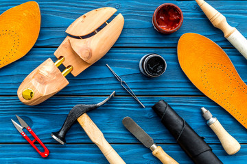 Instruments and materials for make shoes. Shoemaker's work desk. Hummer, awl, knife, sciccors, wooden shoe, insole, paint and leather. Blue wooden background top view pattern