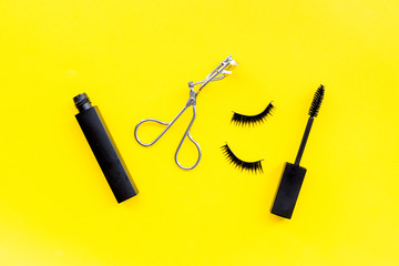 Makeup set for expressive eyelashes. Mascara, false eyelashes, eyelash curler on yellow background top view
