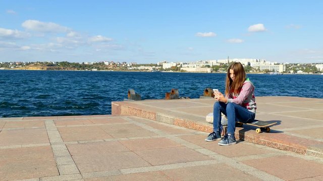 The girl sits on the quay and makes selfy.