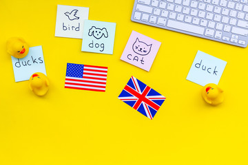 Teach english to a child. Funny english. British and american flags, computer keyboard, stickers with vocabulary, toy duck on yellow background top view copy space