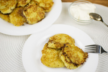 Fried potato pancakes on a white plate and sour cream.