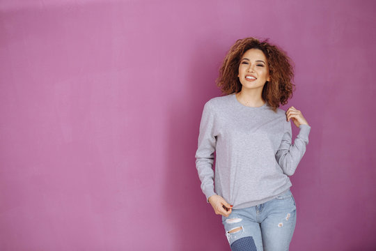 Curly haired girl with freckles in blank grey sweatshirt on violet background. Mock up.