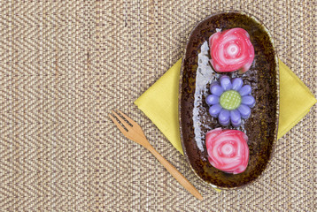 Colorful Thai layer cake in flower shape in design plate with wooden fork on design Jute texture...