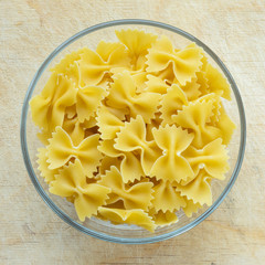 farfalle macaroni pasta in a glass bowl on a wooden table texture background, in the center close-up with the top.