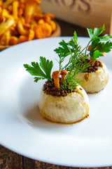 Baked stuffed onions and chanterelles on a white plate close-up