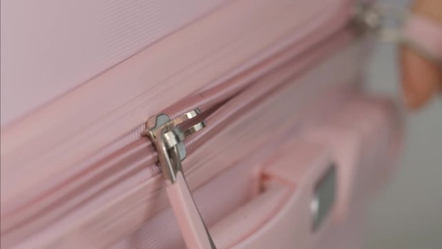 Macro close-up shot of a suitcase's zipper being opened and closed by female fingers