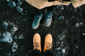 Couple in a hiking boots stand on black sand. Iceland. Top view