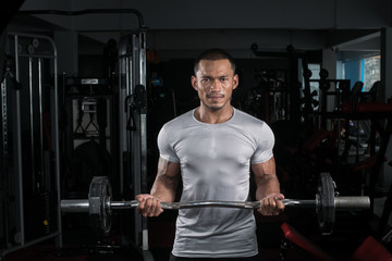 Plakat Muscular builder man training his body with barbell in Modern fitness center