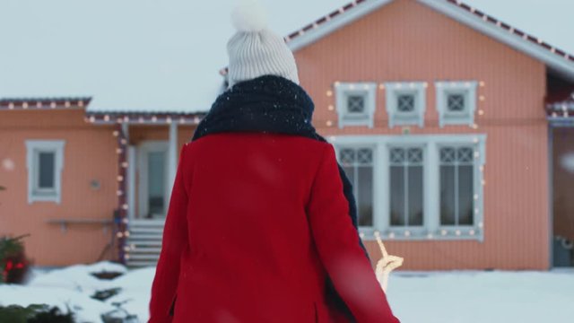 One Winter Day Beautiful Young Woman in the Red Coat Returns Home, She Walks Through Her Backyard into Her Idyllic House. Soft Snow is Falling. Shot on RED EPIC-W 8K Helium Cinema Camera.
