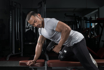 Fototapeta na wymiar Muscular builder man training his body with dumbbell in Modern fitness center