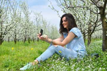 Girl texting on smartphone in a blooming orchid. Beautiful woman enjoy in nature in spring
