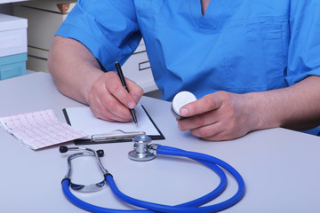 The doctor holds a blister with pills in his hand and writes out the prescription in the workplace close-up. prescribe medicines, a legal pharmacy store, treatment of diseases