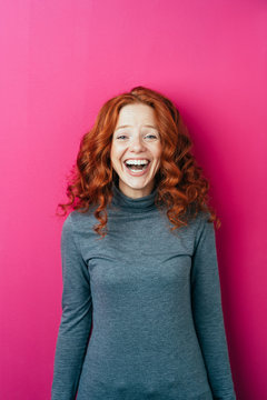 Laughing red haired woman standing in front of a pink background