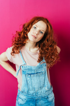 Young red-haired woman standing on pink background