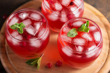 Cranberry refreshment cocktail with mint leaves and ice cubes on the wooden cutting board.