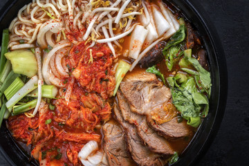 Traditional Korean kimchi jjigae with grilled pork belly and ramen as top view in a pot
