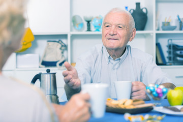 Smiling elderly man drinking tea and talking with woman