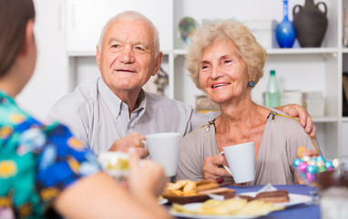Smiling elderly spouses enjoying tea with girl