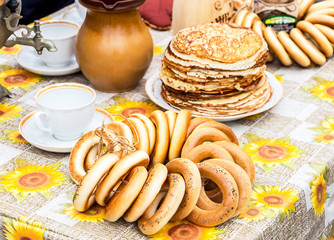 Appetizing tasty bagels, stack of fried pancakes, samovar and tableware
