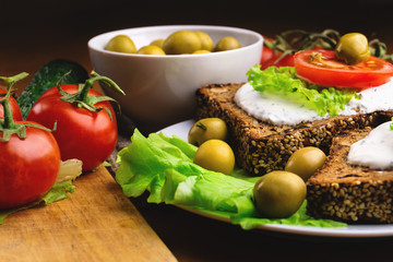 Sandwiches with healthy rye bread, cheese cream, tomatoes, green olives and lettuce on table. Healthy vegetarian food concept