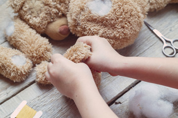 A girl sews a bear toy. Handicraft with children. Child fills the toy with a sintepon. - obrazy, fototapety, plakaty