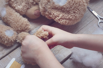 A girl sews a bear toy. Handicraft with children. Child fills the toy with a sintepon. Toning - obrazy, fototapety, plakaty