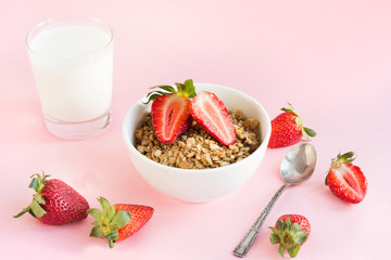 Healthy breakfast of granola, strawberry and milk on pink.