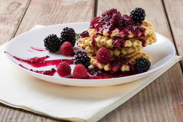 Belgian waffles with berries and jam in a plate on a wooden table