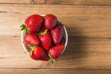 White bowl with some strawberries on a wooden table
