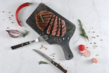 On a dark wooden board a juicy steak cooked on the grill. In the frame cutlery, fresh radish,...