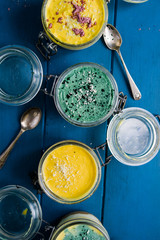 Cheesecake on a glass jar, made with mango and spirulina powder, with chia seeds and coconut powder, over a wooden blue background