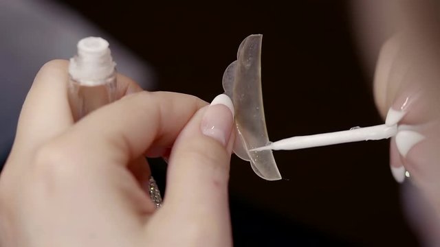 lash lamination master is coating a silicon roller by glue and applying it on a upper eyelid of womans face in a cosmetological salon