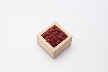 Dried red goji berries in the wooden square cup isolated
