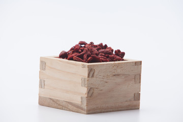 Dried red goji berries in the wooden square cup isolated
