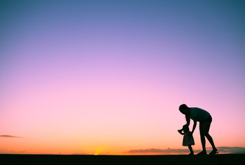 Silhouette of mother and her little toddler playing together. Parenting and family life concept.  
