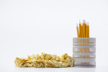 Crumpled yellow papers with pencils pot on white