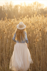 Happy young pretty girl in a hat run in a field at sunset	