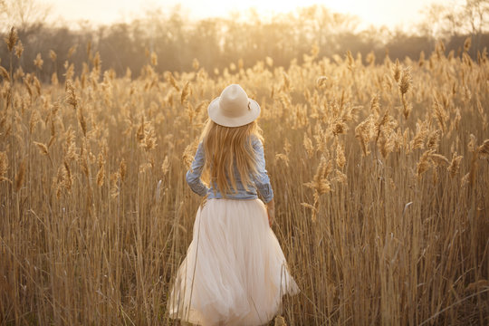 Happy young attractive girl in a hat run in a field at sunset. having fun,expressing positivity, joy, happiness
