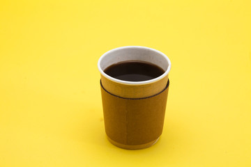 Black coffee in cardboard throwaway coffee cup on yellow 