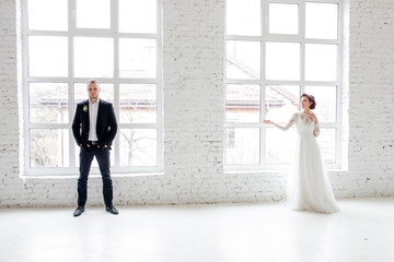 The bride and groom dancing by the big window in the studio with a white interior.