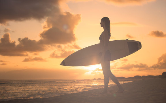 Surfer girl walking on beach during a beautiful sunset. 