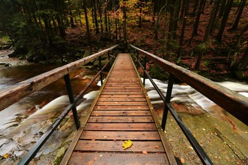 Wooden old bridge across the Mumlava River, in autumn forest environment