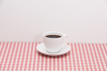 A cup of coffee on red and white checkered table 
