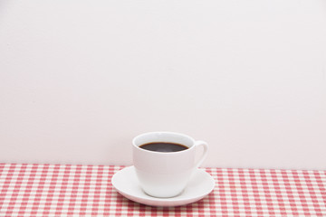 A cup of coffee on red and white checkered table 