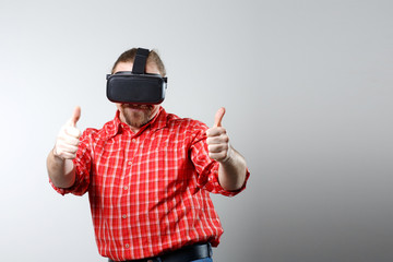 Portrait of bearded man watching virtual reality glasses over gray background with copyspace.