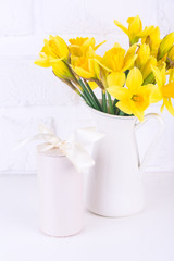 Jar with narcissuses and a gift box at the white background. Spring, mothers day and easter concept