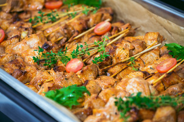 Fresh grilled pork shish kebab served with tomato cherry and greens on skewers on hot plate