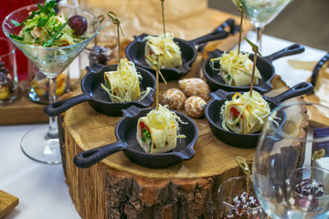 Beautiful decorated catering banquet table with different food snacks and appetizers. Canape rolls in small pans on wood