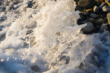 pebble stones on the sea beach, the rolling waves of the sea with foam